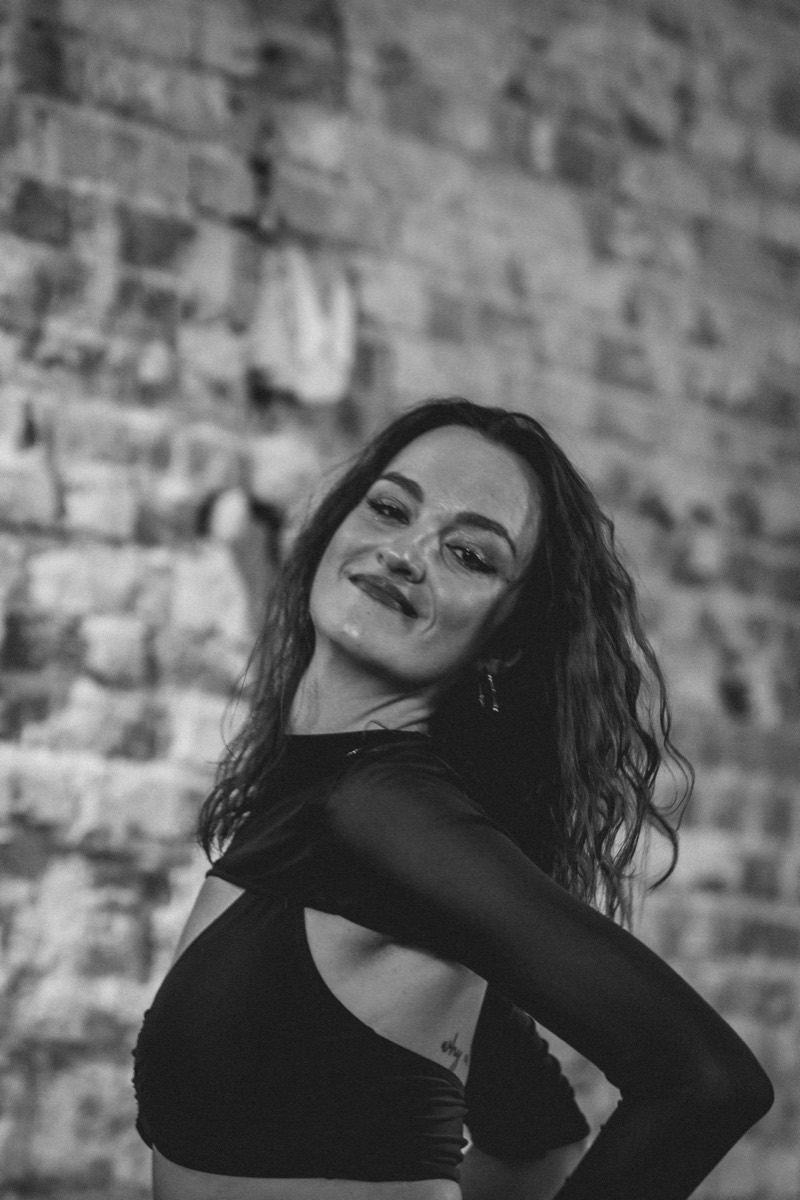 Black-and-white portrait of Wiktoria smiling, against a brick wall