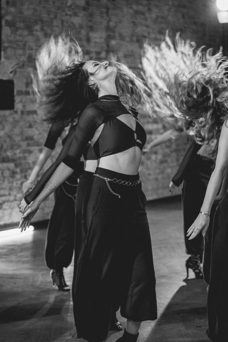 Black-and-white photo of Wiktoria dancing with a group, hair flying in motion